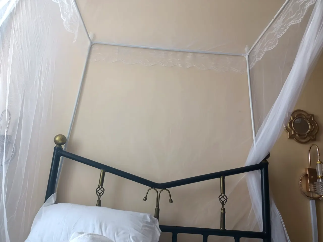 Wrought-iron headboard with brass finials under a lace canopy