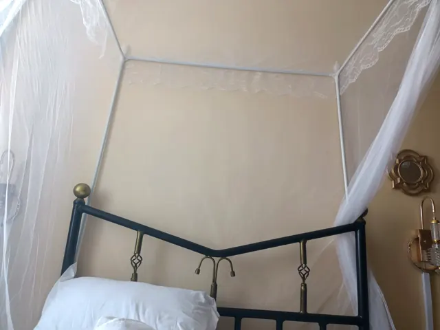Wrought-iron headboard with brass finials under a lace canopy